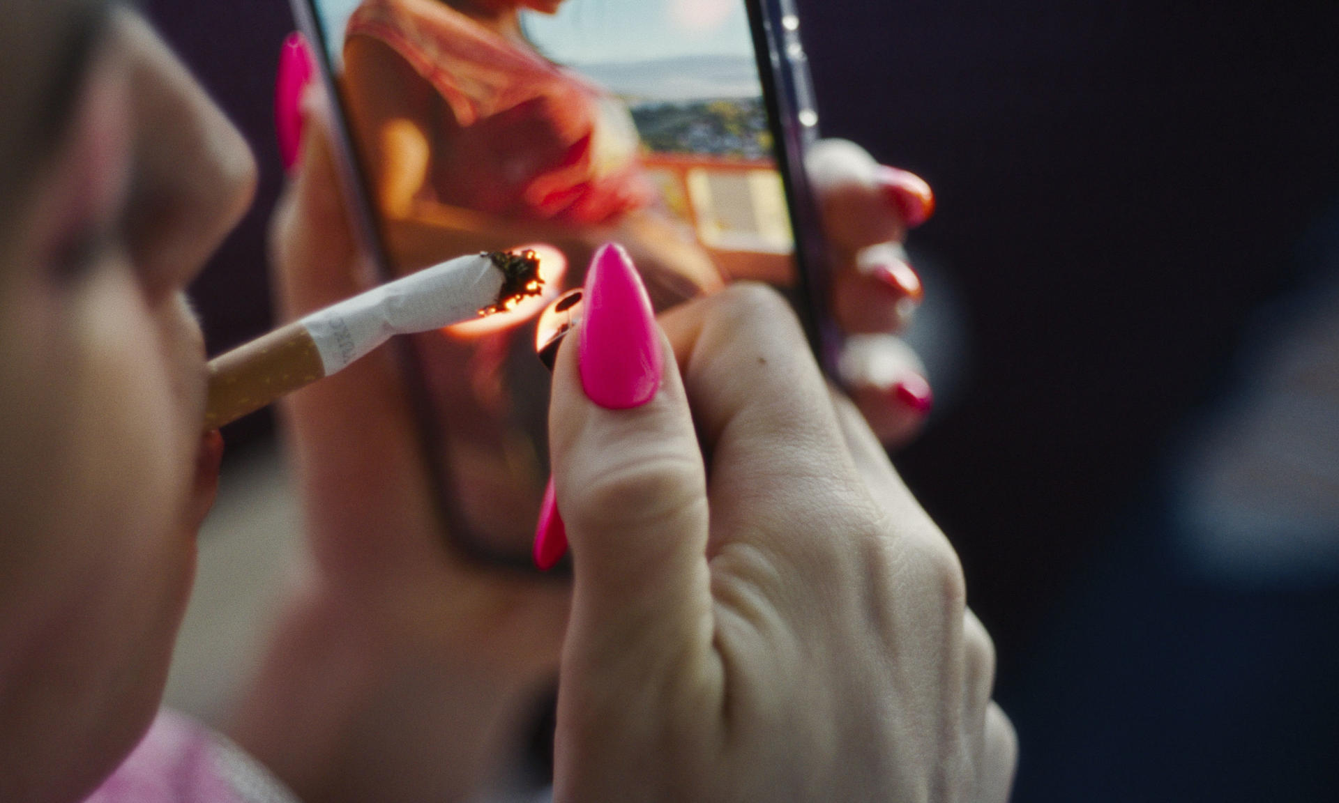 Frau zündet Zigarette an, während sie ein Bild auf dem Handy betrachtet.