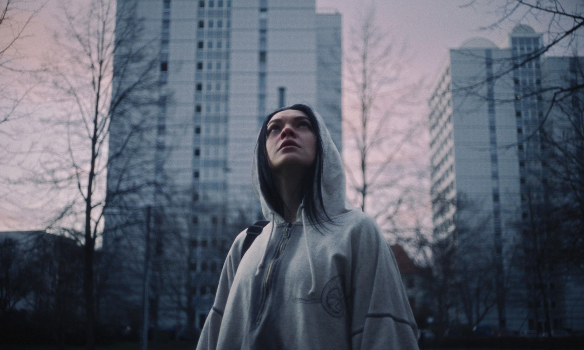 Eine Person in einem Kapuzenpullover blickt zu hohen Gebäuden und zum Himmel auf.