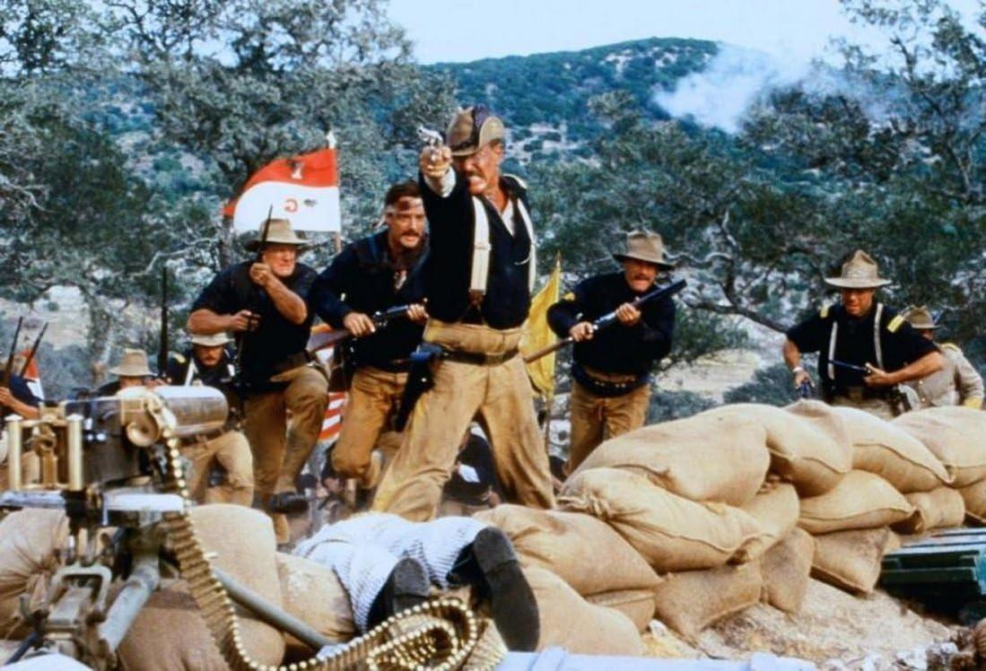 Eine historische Kampfszene mit uniformierten Soldaten, die Waffen abfeuern, und Sandsäcken im Vordergrund.
