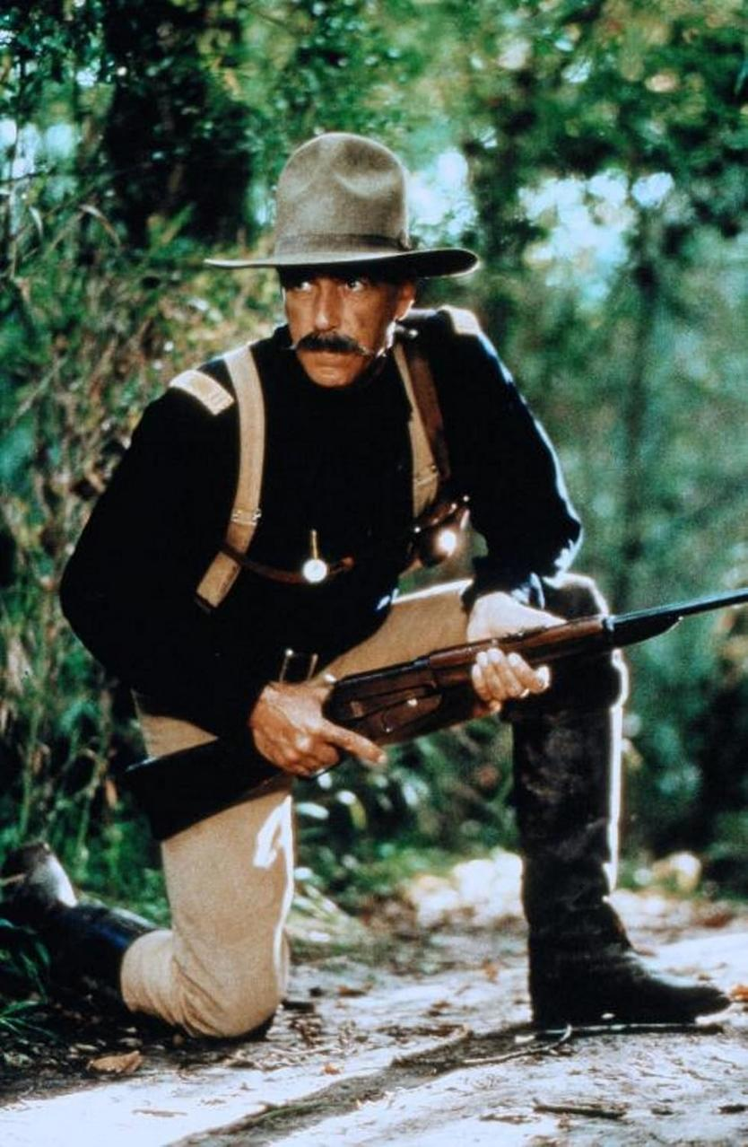 Mann in Militäruniform kniend in einem Wald, der ein Gewehr hält.
