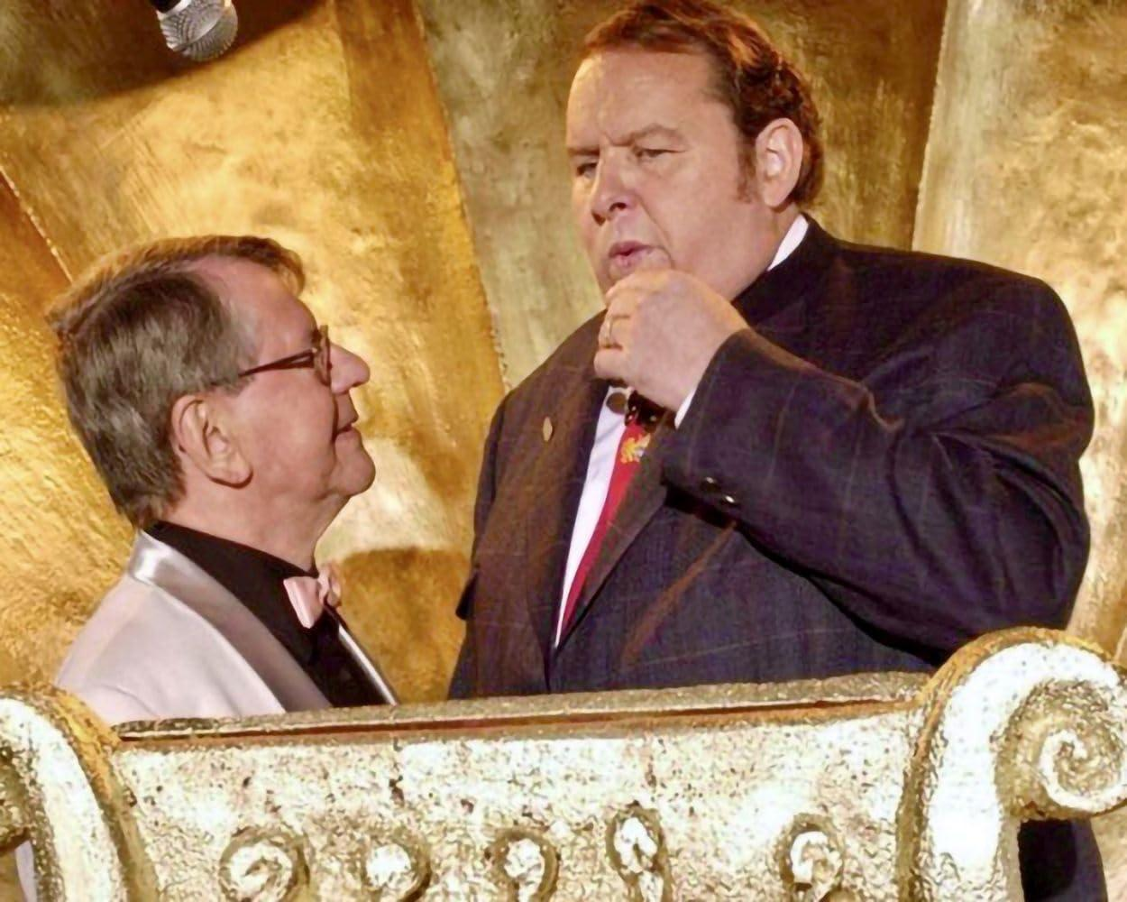 Zwei Männer in Anzügen unterhalten sich, goldener Hintergrund.