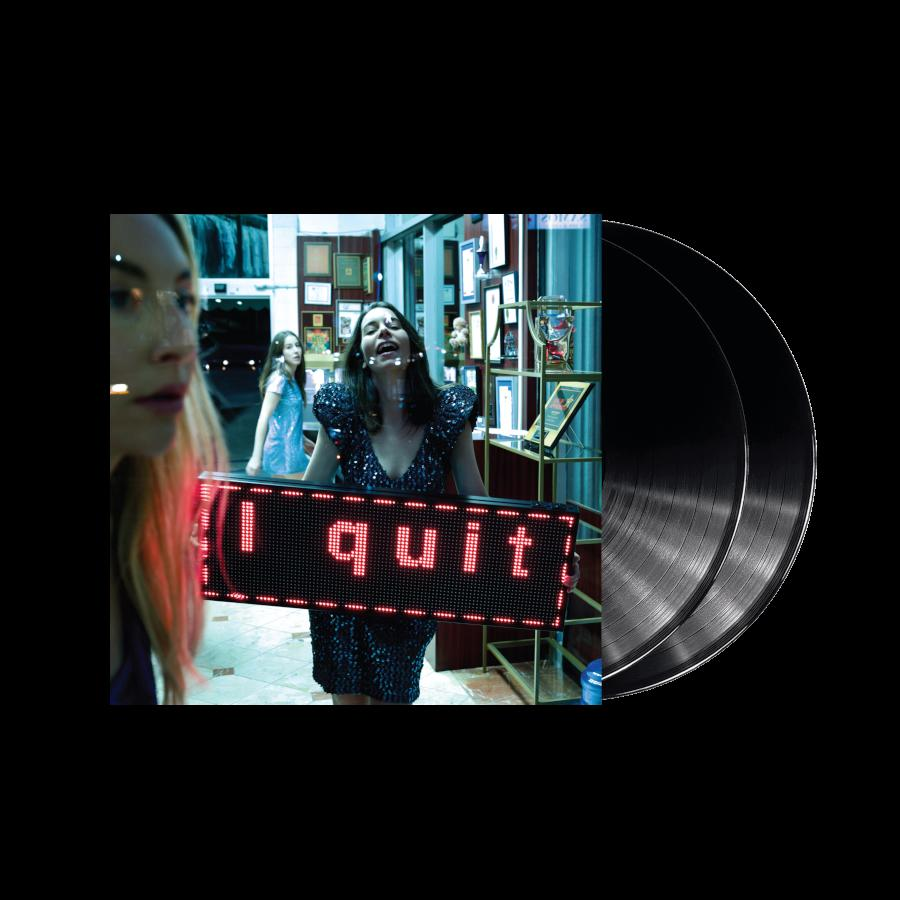 Frau vor einem beleuchteten Schild mit der Aufschrift „I quit“ mit schwarzen Schallplatten rechts.