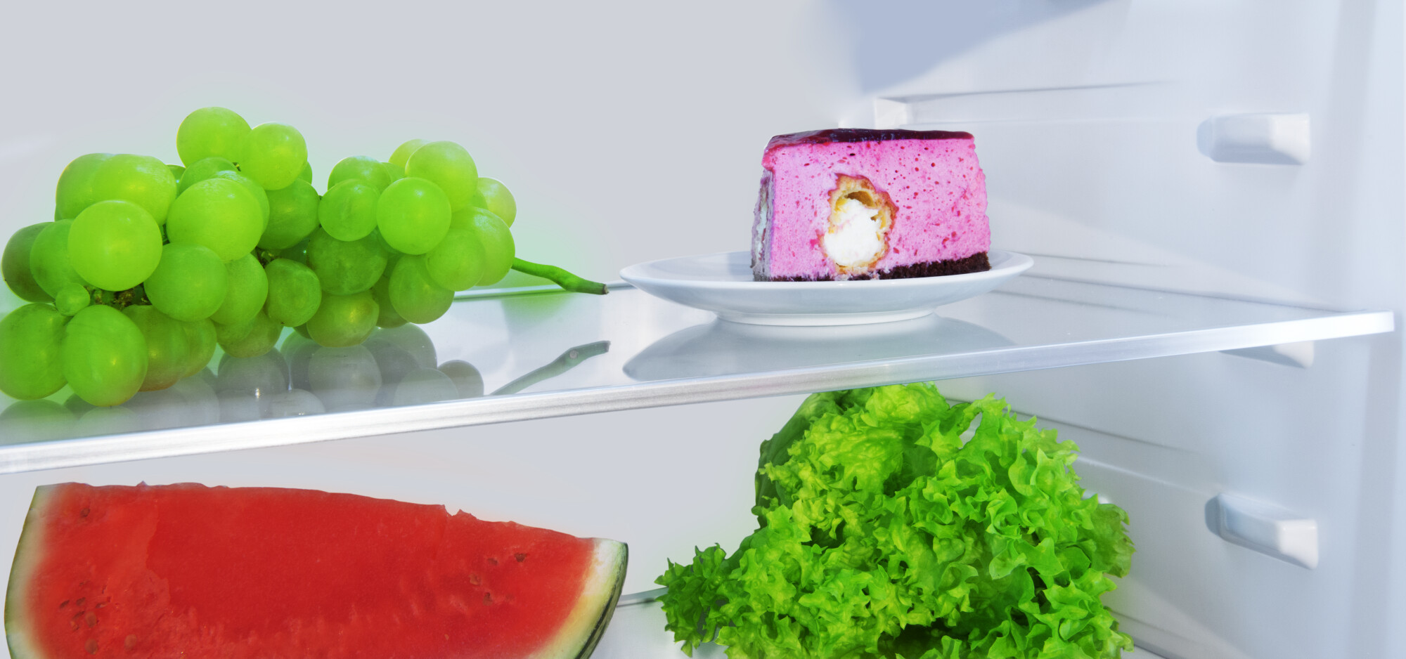 In einem Kühlschrank mit Trauben, Kuchen, Wassermelone und Salat.