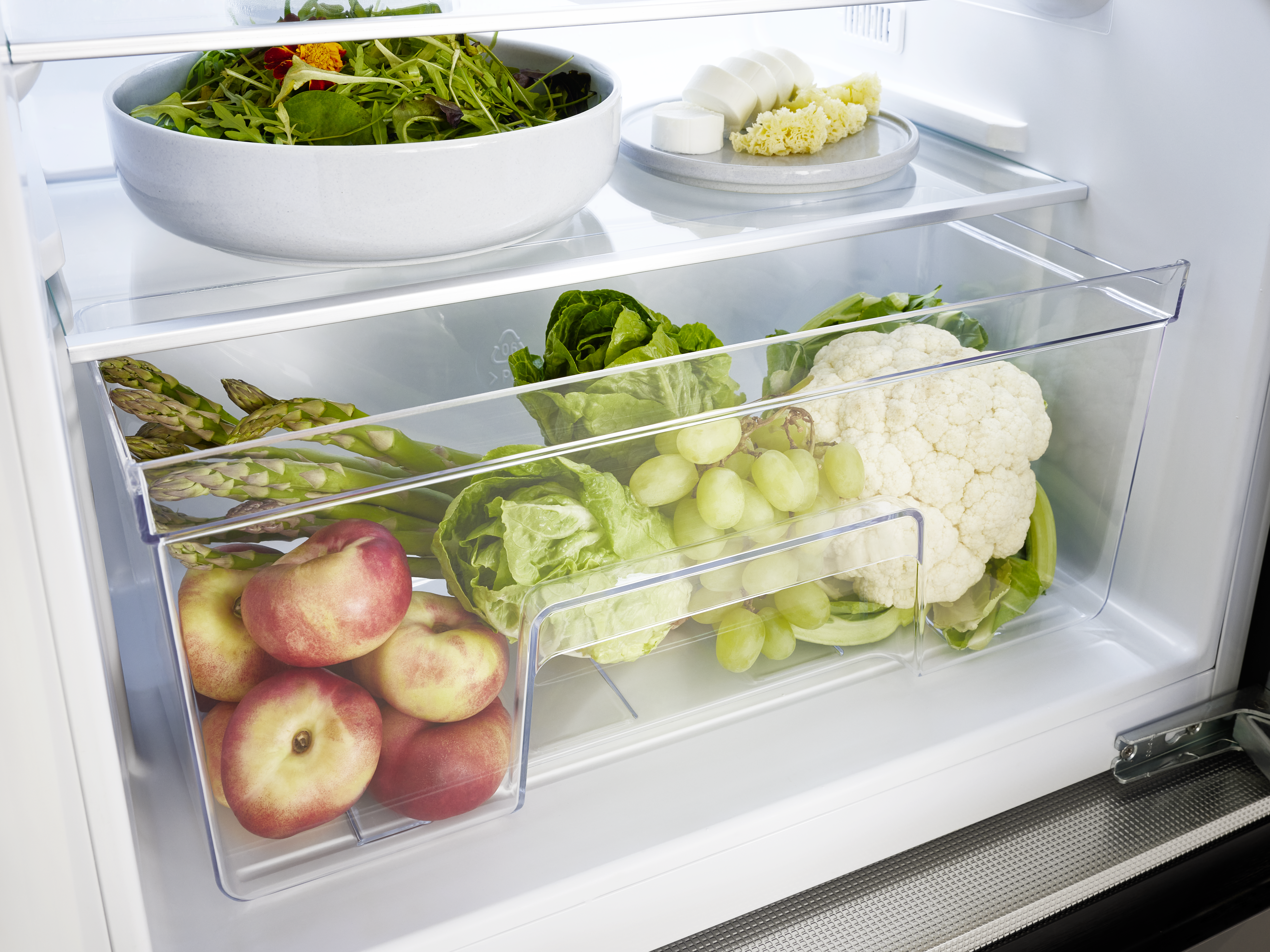 Kühlschrank-Innenraum: Frische Lebensmittel wie Salat, Pfirsiche, Trauben und Blumenkohl.