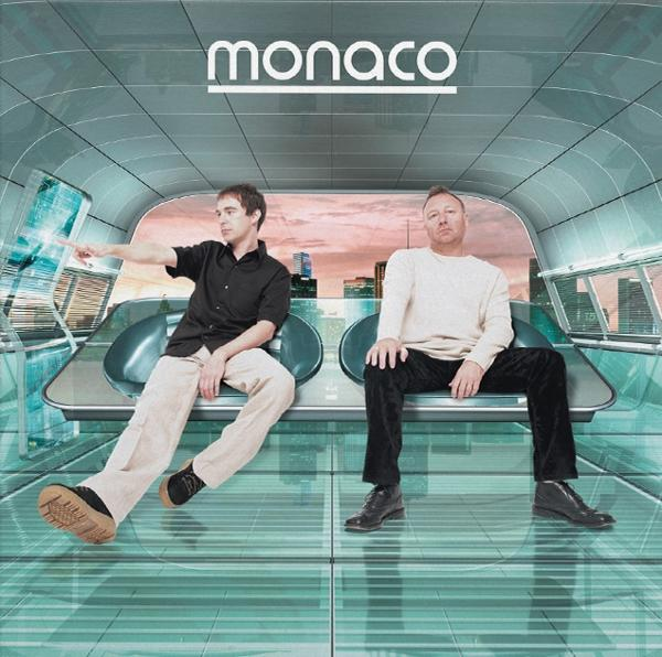 Zwei Männer sitzen in einem futuristischen Innenraum. Über ihnen steht das Wort "monaco".