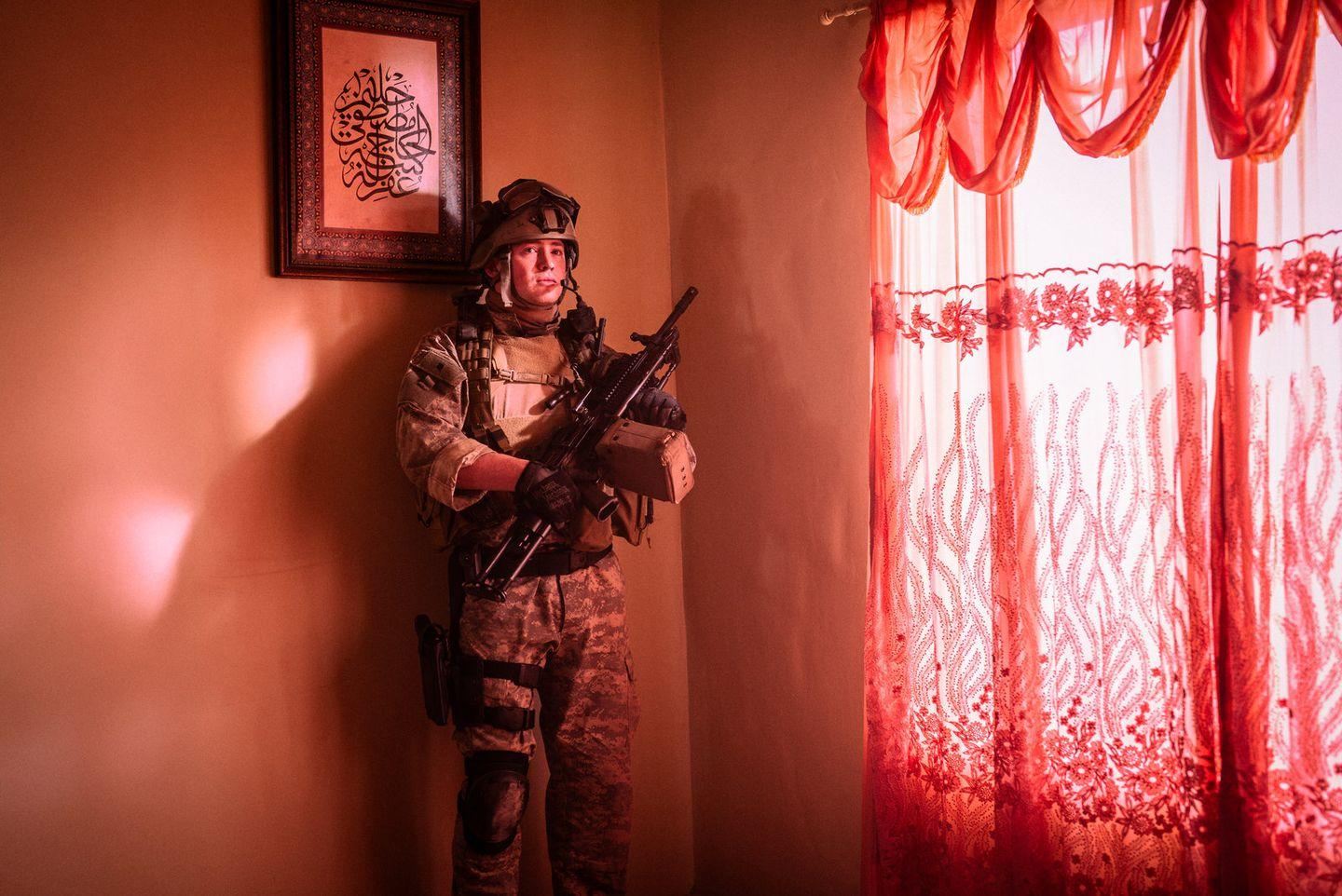 Soldat mit einer Waffe steht in einem Raum. Ein Bild hängt an der Wand, ein roter Vorhang ist zu sehen.