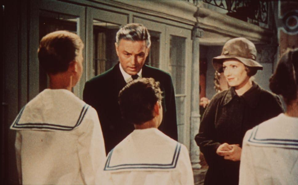 Filmszene: Gruppe von Menschen vor einem Gebäude, mit einer Familie im Fokus.
