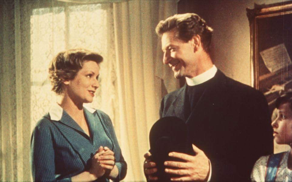 Filmstill. Mann und Frau in einem Raum. Mann im Kragen. Gemälde an der Wand. Lächeln.