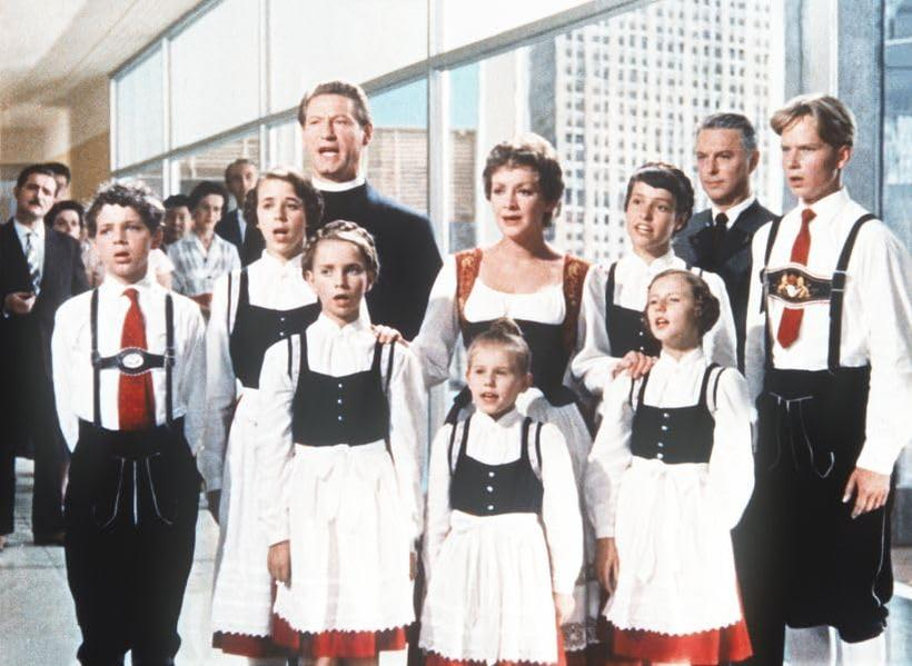 Eine Gruppe von Menschen, darunter Kinder, in traditioneller österreichischer Tracht, singt in einem Gebäude.