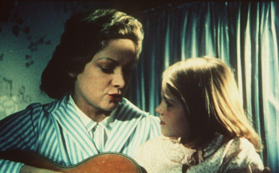 Eine Frau spielt Gitarre und singt für ein junges Mädchen. Die Szene ist drinnen.