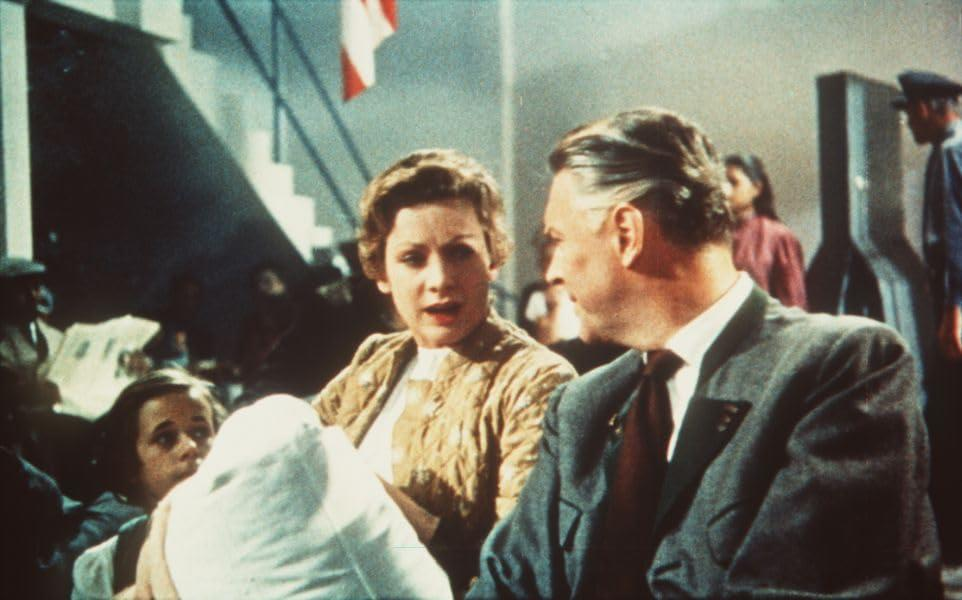 Eine Szene aus einem Film. Ein Mann und eine Frau unterhalten sich. Andere im Hintergrund.