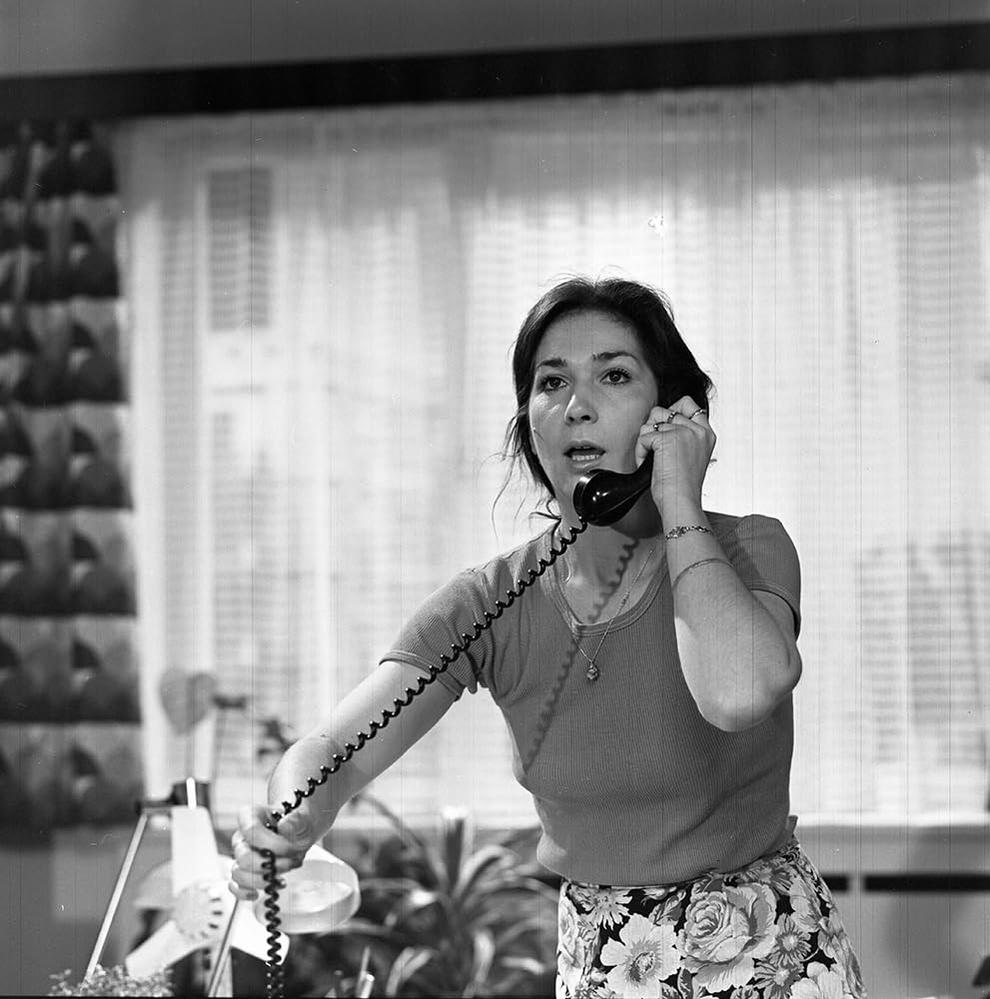 Frau telefoniert besorgt, mit Blumenrock und schwarzem Telefonkabel.