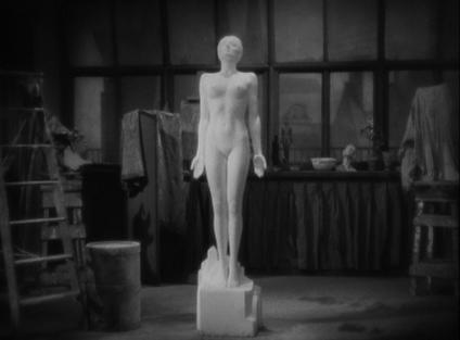Schwarz-Weiß-Foto einer nackten Statue in einem Atelier. Die Statue steht auf einem Sockel.