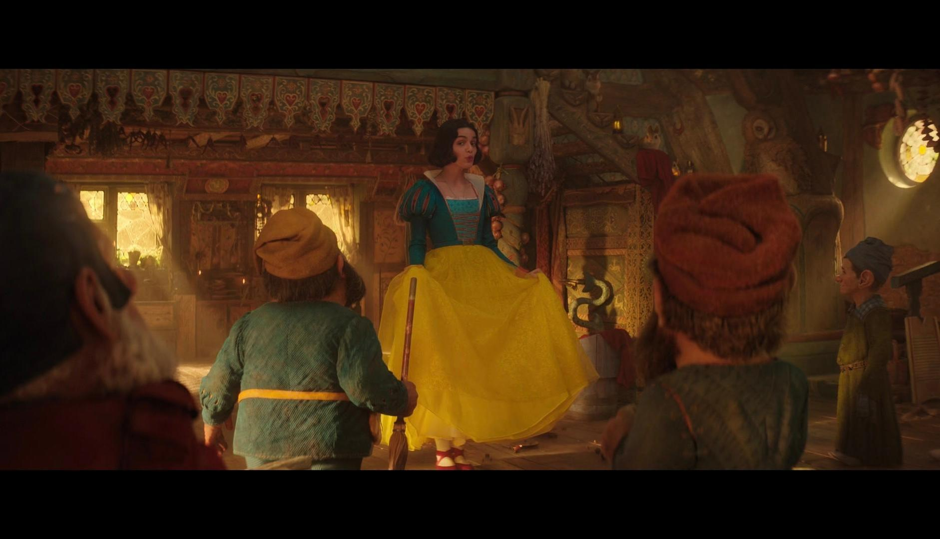 Filmszene: Schneewittchen in gelbem Kleid, umgeben von Zwergen.