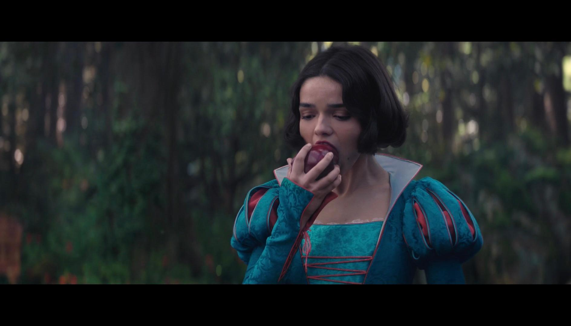 Szene aus einem Film. Eine Frau in blauem Kleid isst einen Apfel im Wald. Dunkler Hintergrund.