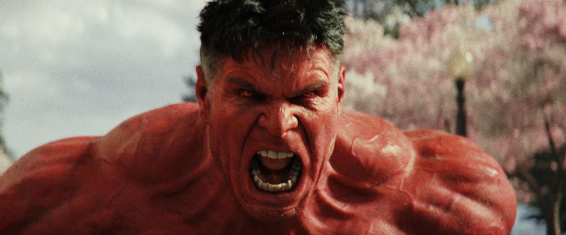 Der Rote Hulk schreit. Sein Gesicht ist rot und verzerrt. Der Hintergrund sind leicht verschwommene Bäume und ein Gebäude.