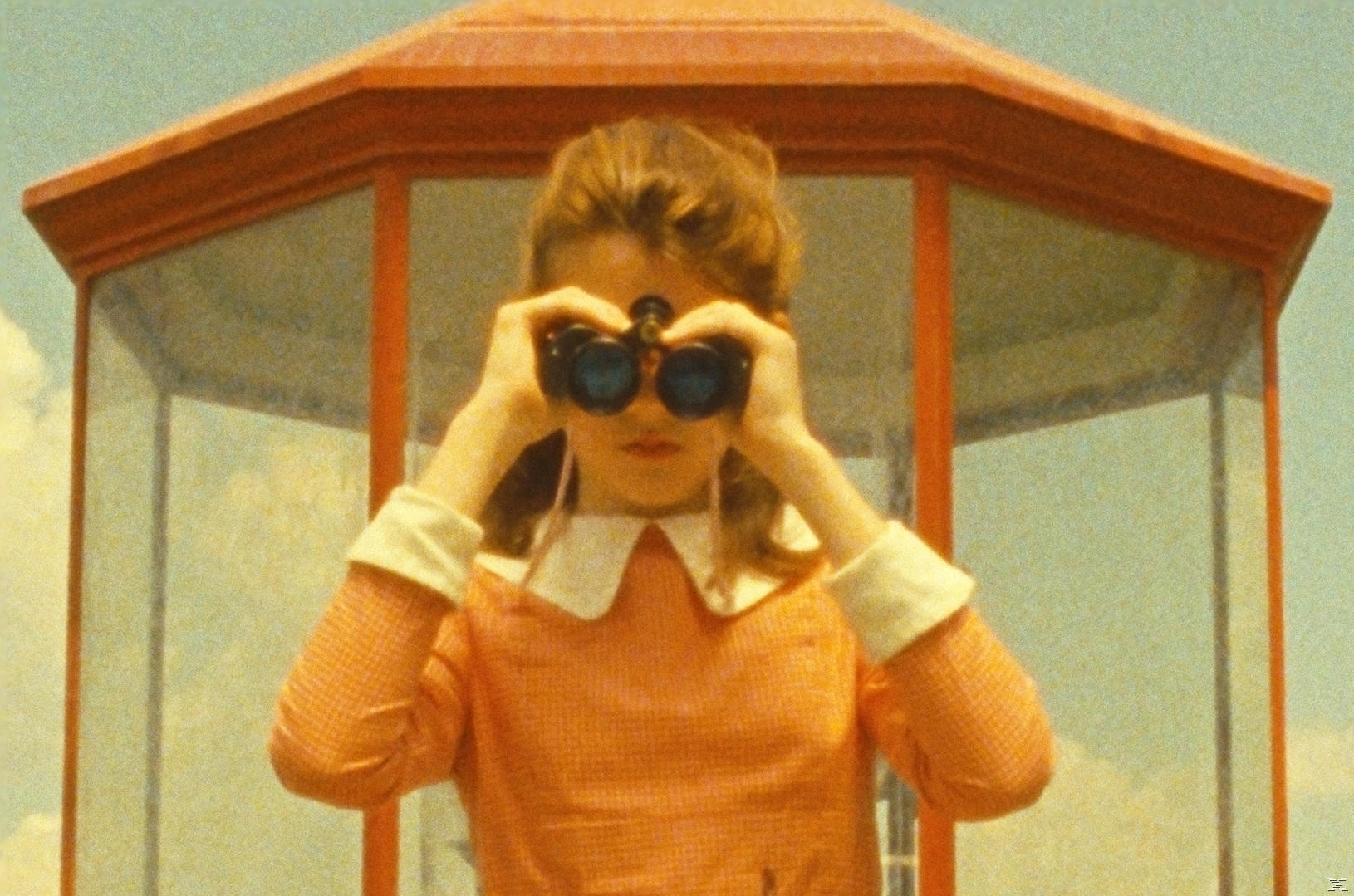 Eine Frau blickt durch ein Fernglas vor einer roten Struktur.