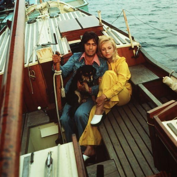 Mann und Frau auf Boot, mit Hund. Meer im Hintergrund.