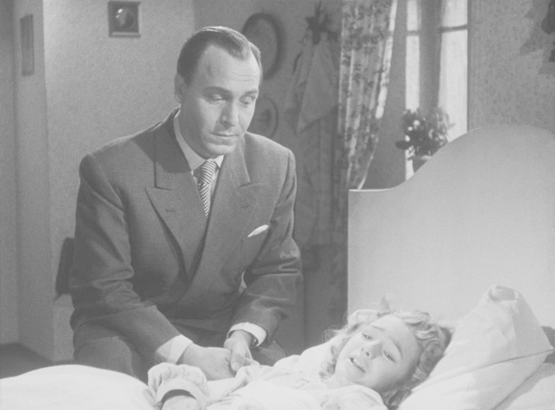 Ein Mann im Anzug beugt sich über ein Kind im Bett, ein klassisches Schwarzweißfoto.