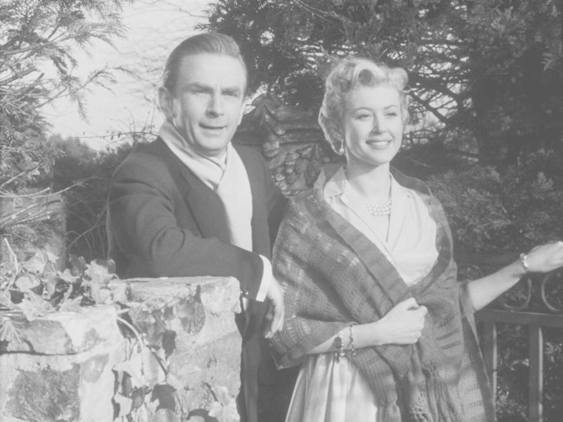 Schwarz-Weiß-Foto eines Mannes und einer Frau, die an einer Steinmauer stehen und lächeln.