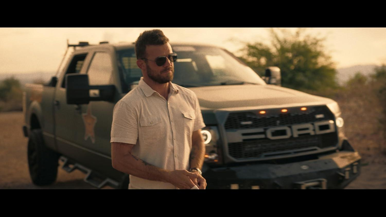 Mann mit Sonnenbrille steht vor einem Truck in einer Wüstenlandschaft.