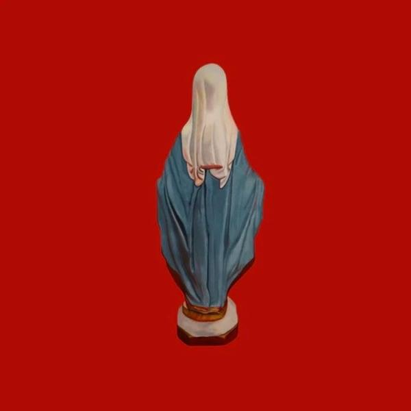 Eine weiße Statue der Jungfrau Maria mit blauem Umhang steht vor rotem Hintergrund.