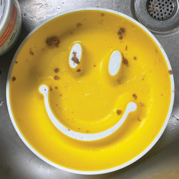 Gelbe Katzenfutter-Schale mit Smiley-Gesicht und Futterresten in einem Waschbecken.