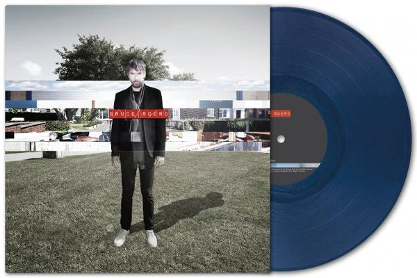 Album-Cover: Mann im Anzug steht auf Gras, blaue Vinyl-Schallplatte sichtbar.