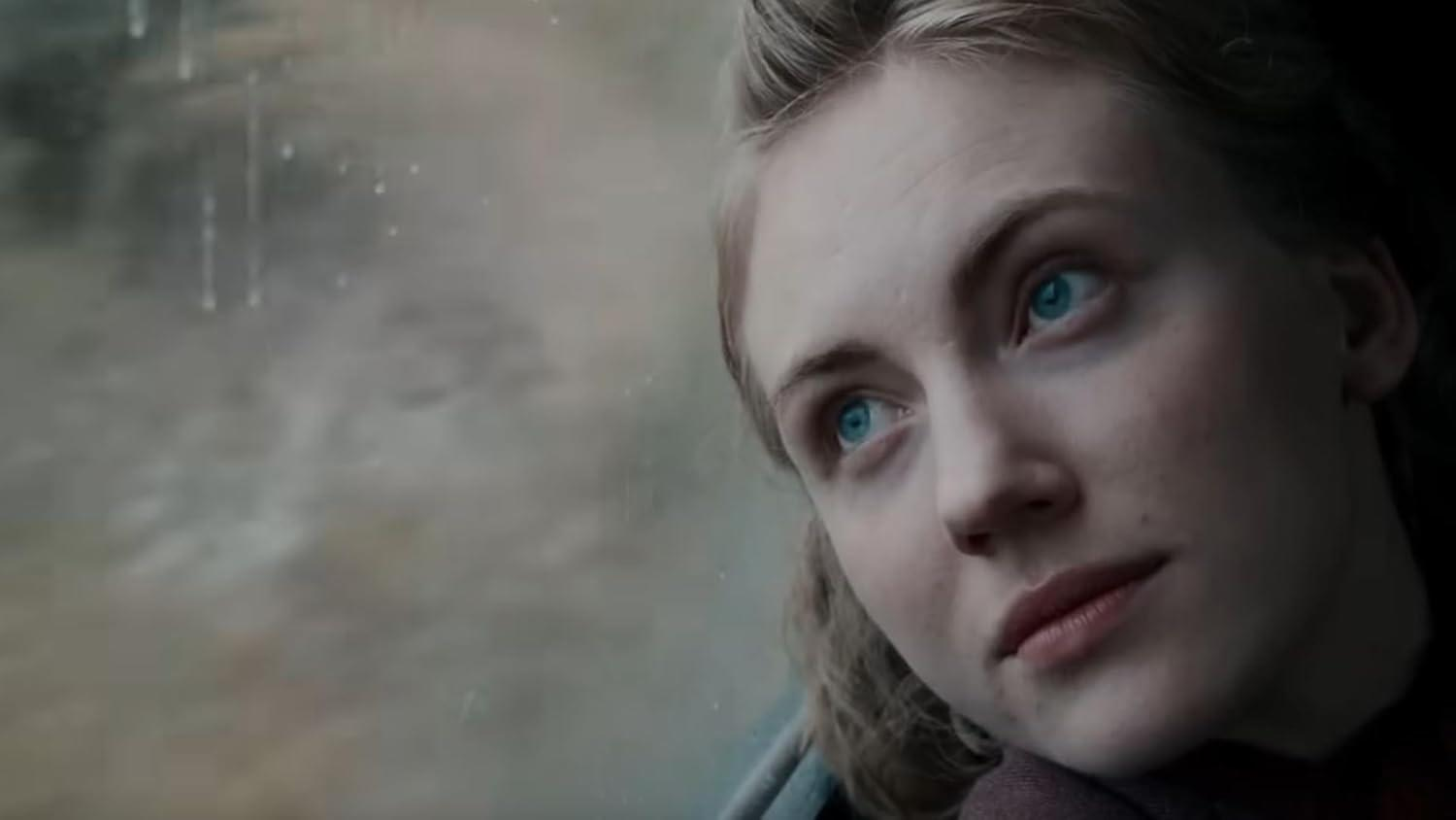 Eine Frau mit blauen Augen schaut aus einem Zugfenster, mit einer verschwommenen Außenszene.