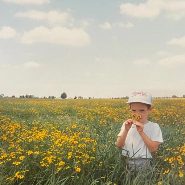 Ein Junge auf einem Feld mit gelben Blumen, der eine Blume an seine Nase hält.