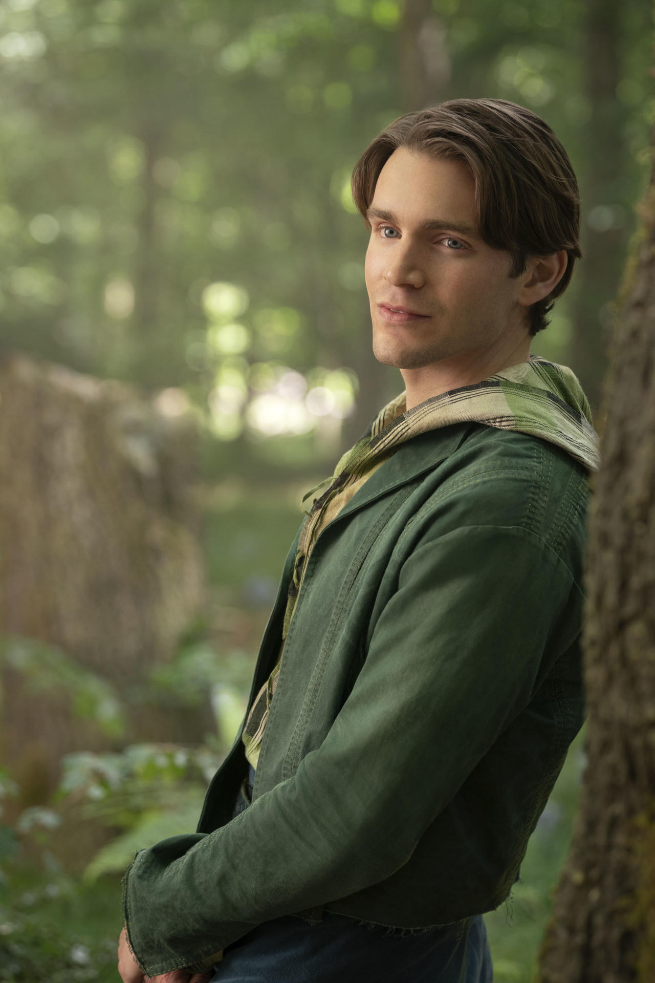 Ein Mann in grüner Jacke steht in einem Wald und schaut in die Kamera. Waldhintergrund.