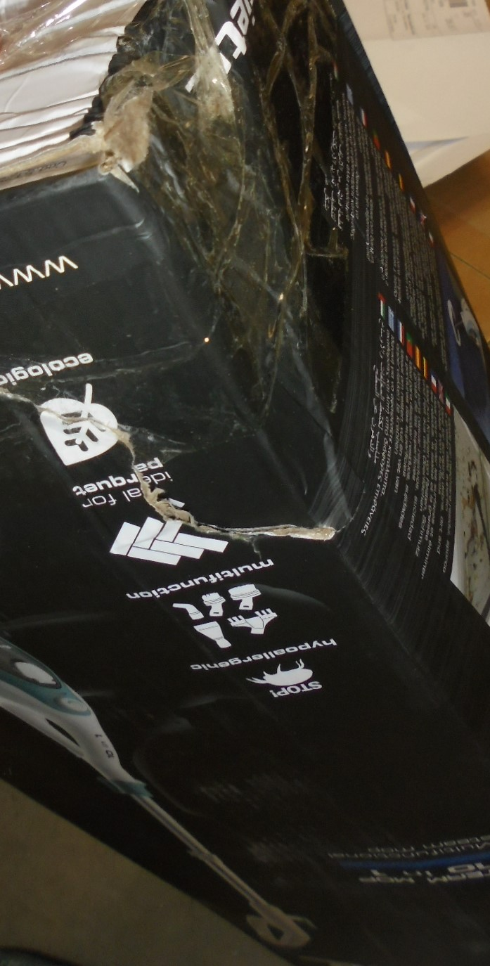 Zbliżenie uszkodzonego, czarnego i przezroczystego pudełka owiniętego folią, z białym tekstem i symbolami.