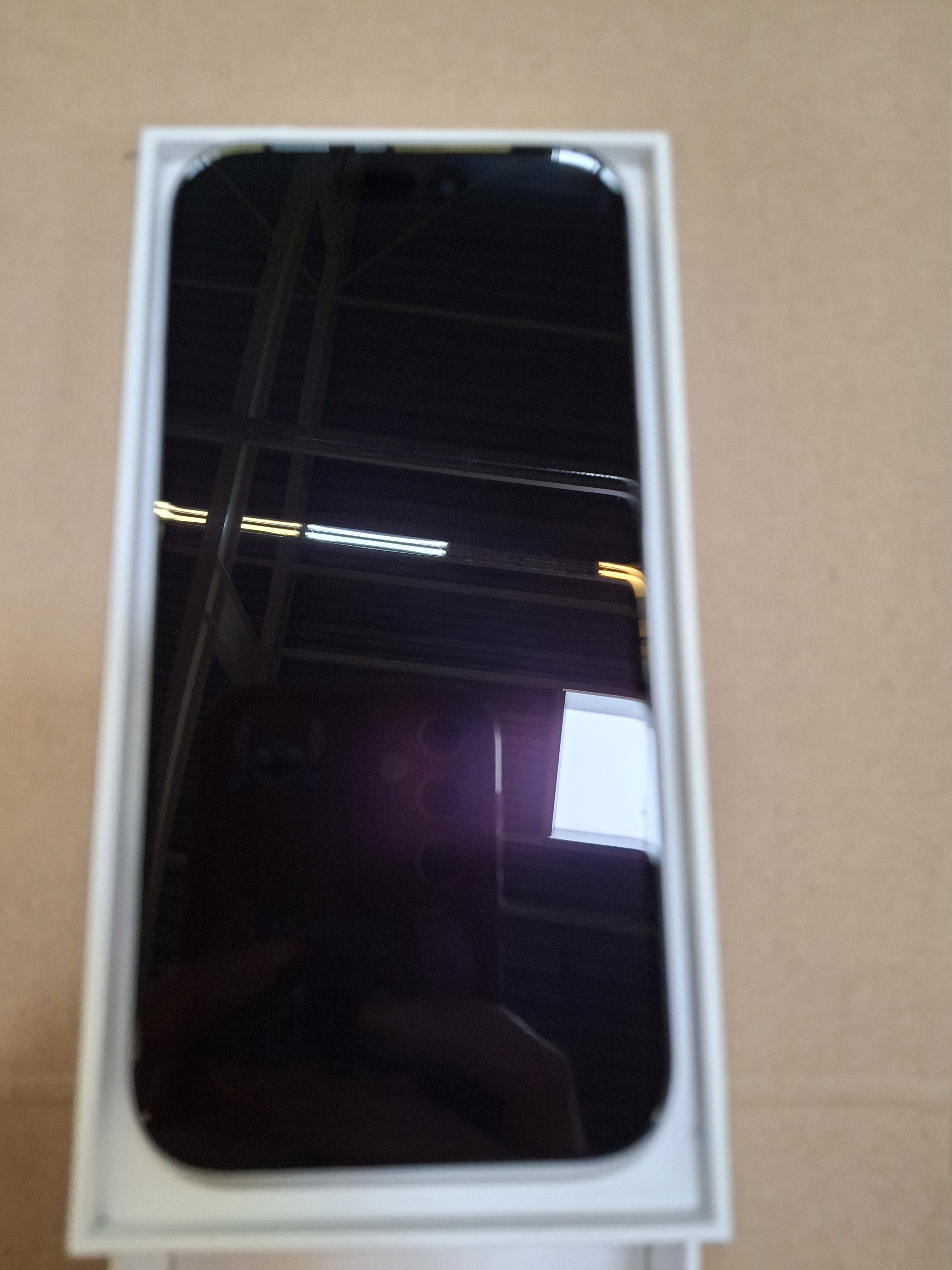 Czarny iPhone w białym pudełku. Ekran jest widoczny i odbija światło.