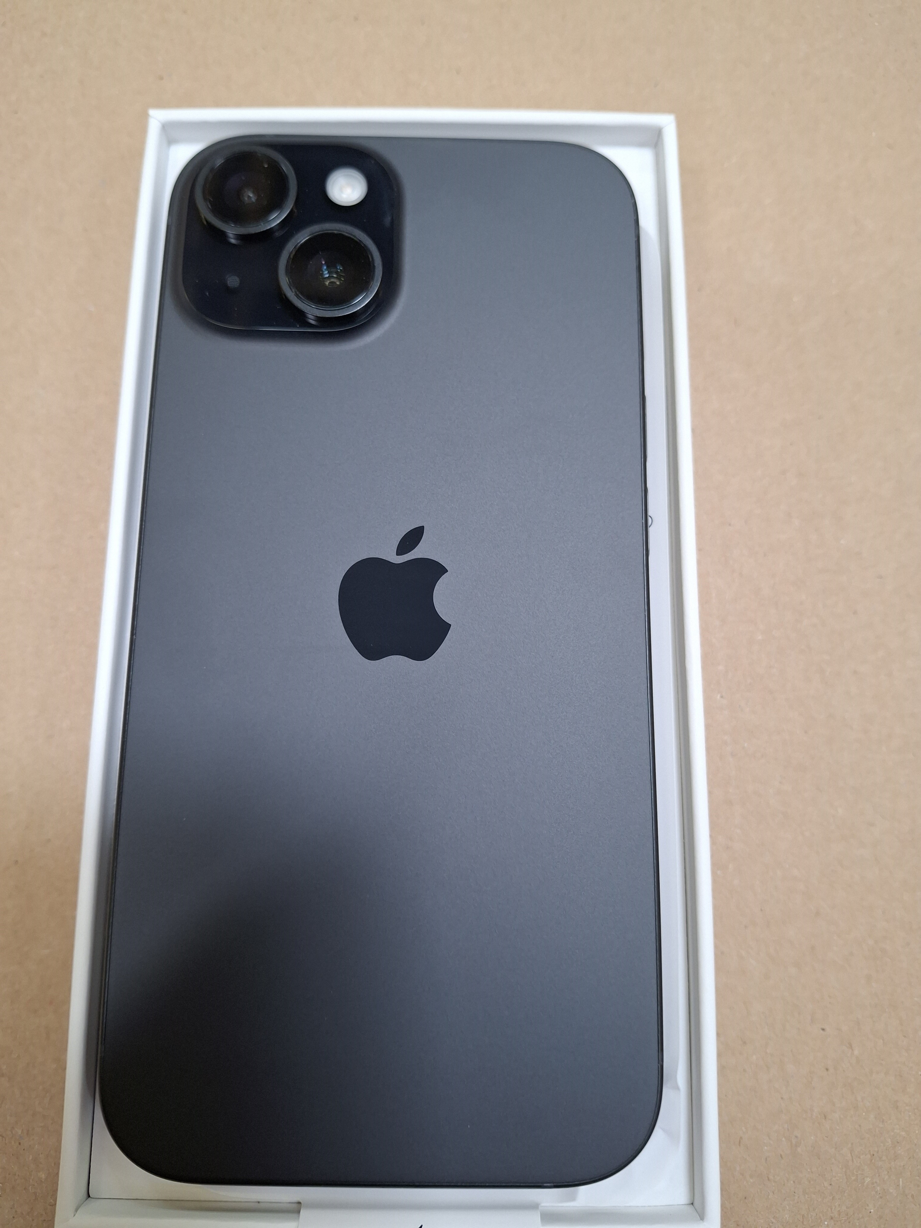 Czarny iPhone z dwoma aparatami na plecach, w białym pudełku. Widoczne jest logo Apple.