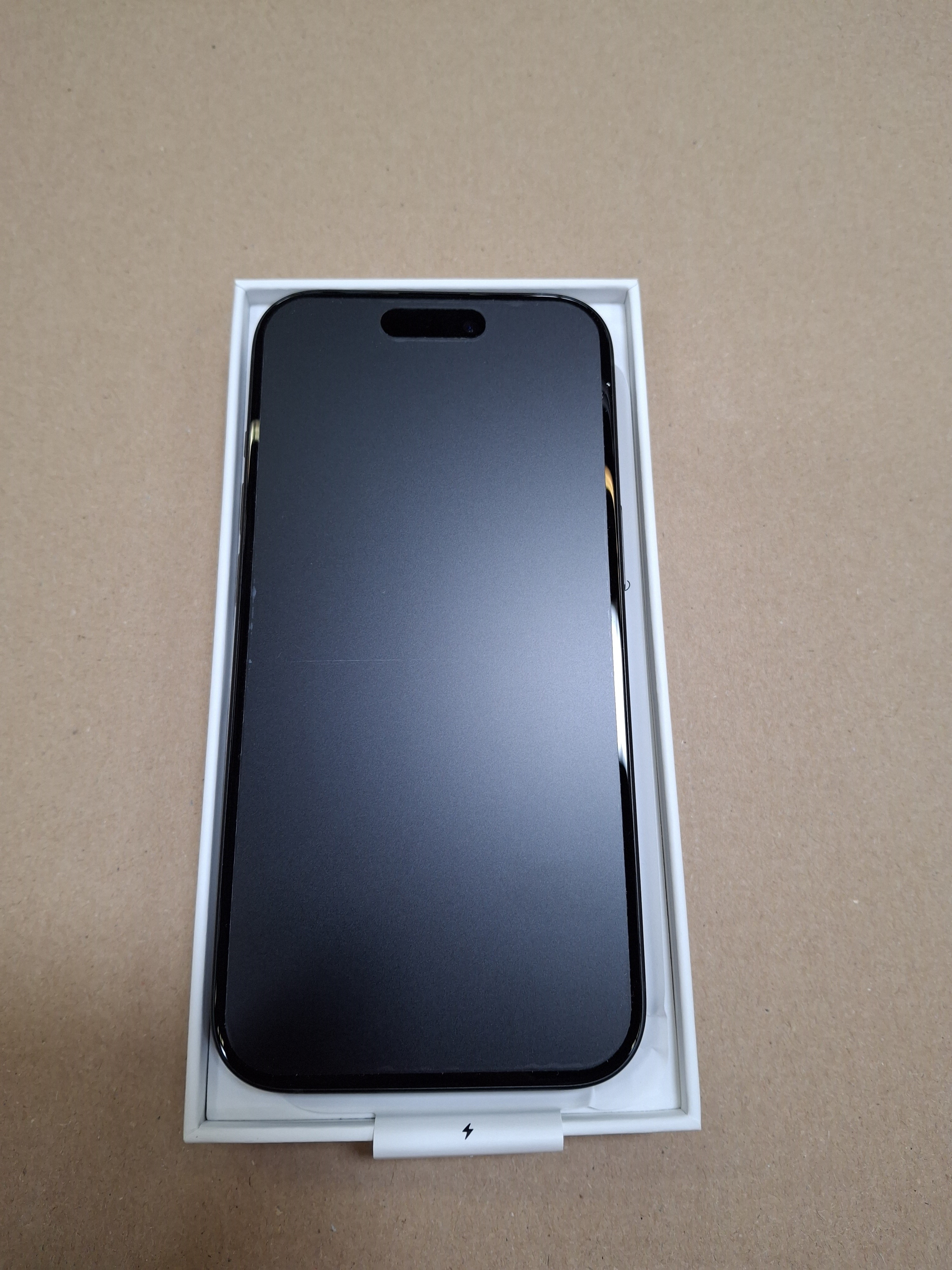 Czarny iPhone w białym pudełku. Ekran jest widoczny i odbija światło.