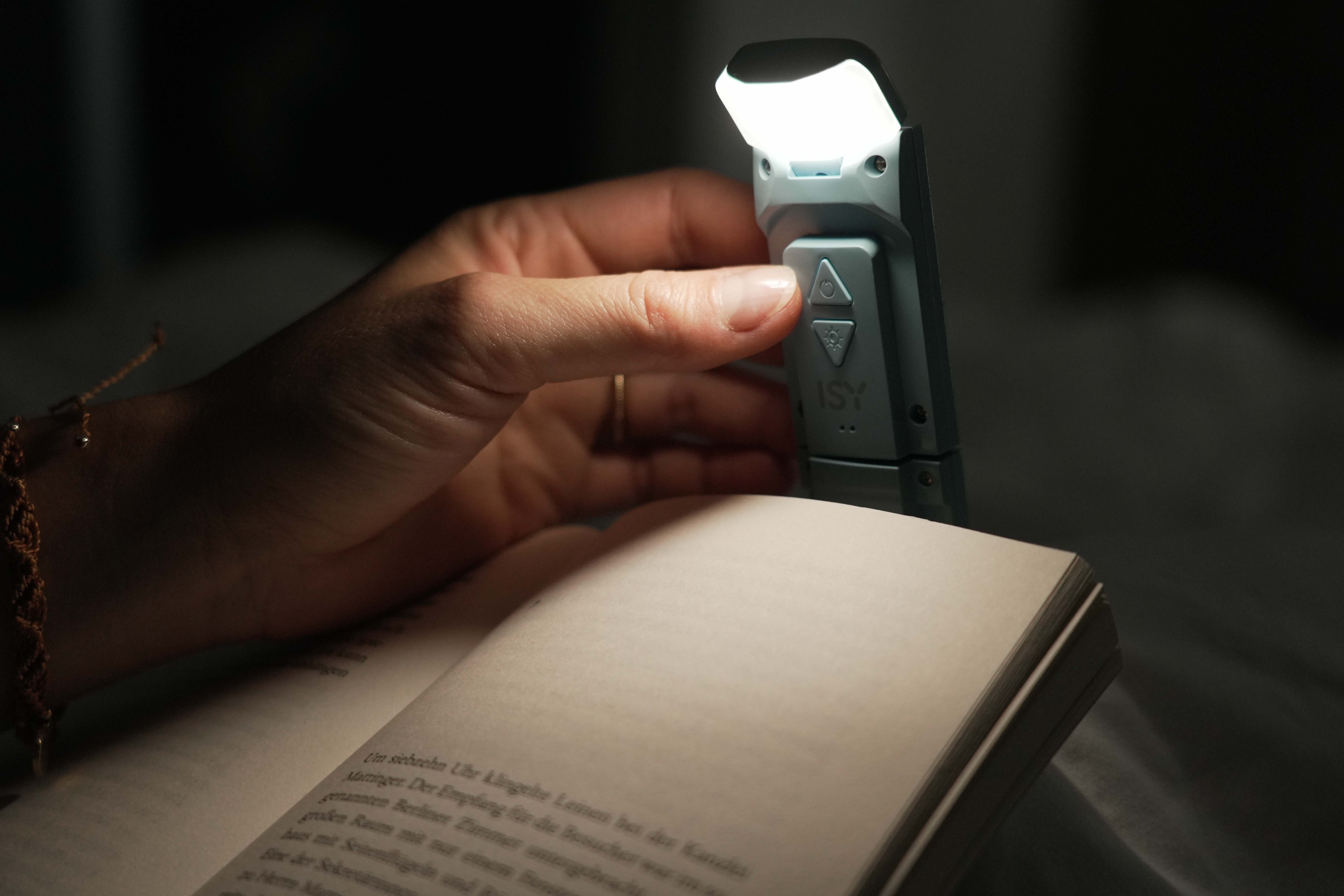 Main tient une lampe de lecture au-dessus d'un livre ouvert.