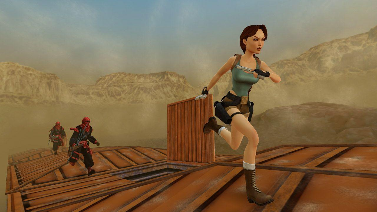Lara Croft rennt auf einer Holzkonstruktion, von Feinden in einer Wüstenlandschaft verfolgt.