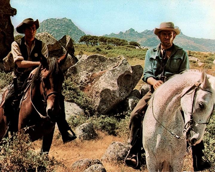 Zwei Cowboys auf Pferden in einer Wüstenlandschaft mit Felsen.
