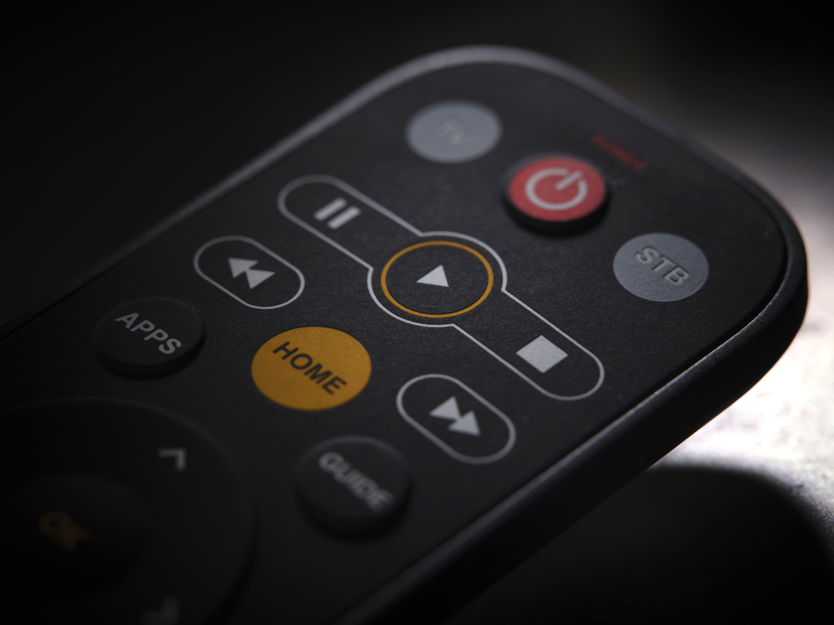 Schwarze Fernbedienung mit verschiedenen Tasten: Power, Home, Play, Apps und Guide. Orange und graue Tasten.