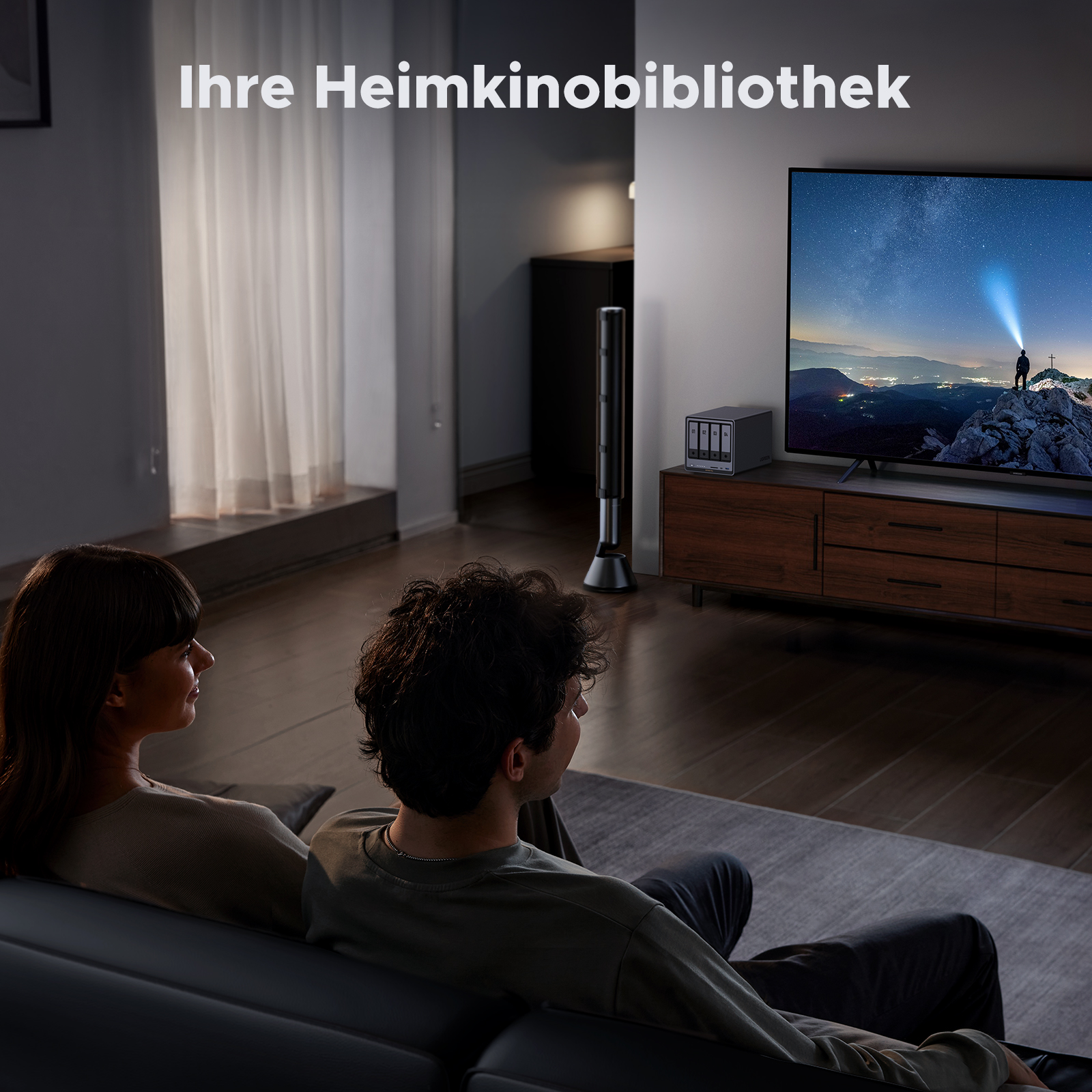 Ein Paar schaut fern. Ein NAS-Gerät ist auf einem Schrank zu sehen. Text: 'Ihre Heimkinobibliothek'.