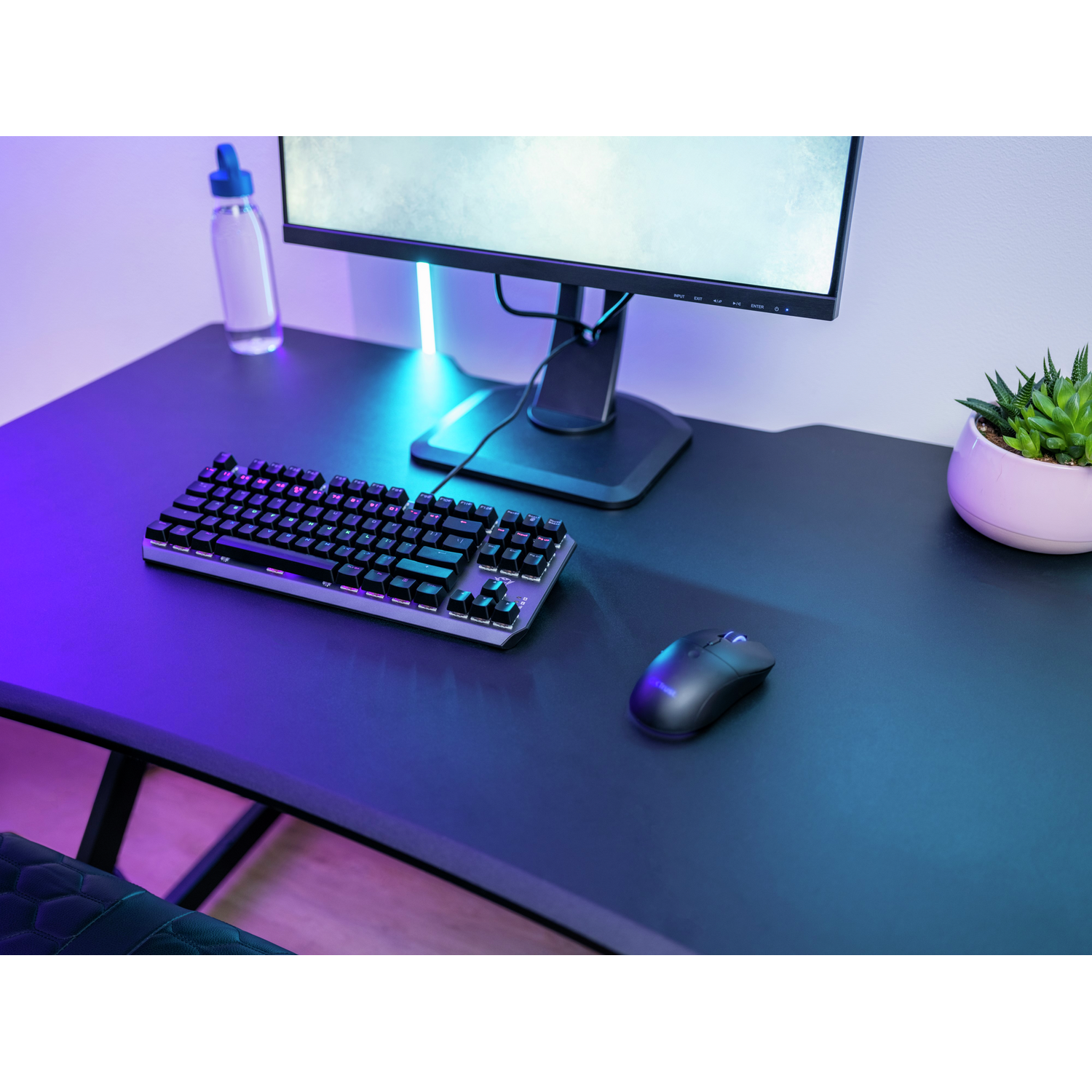 Desk setup with a keyboard, mouse, monitor, and a water bottle, with purple and blue lighting.