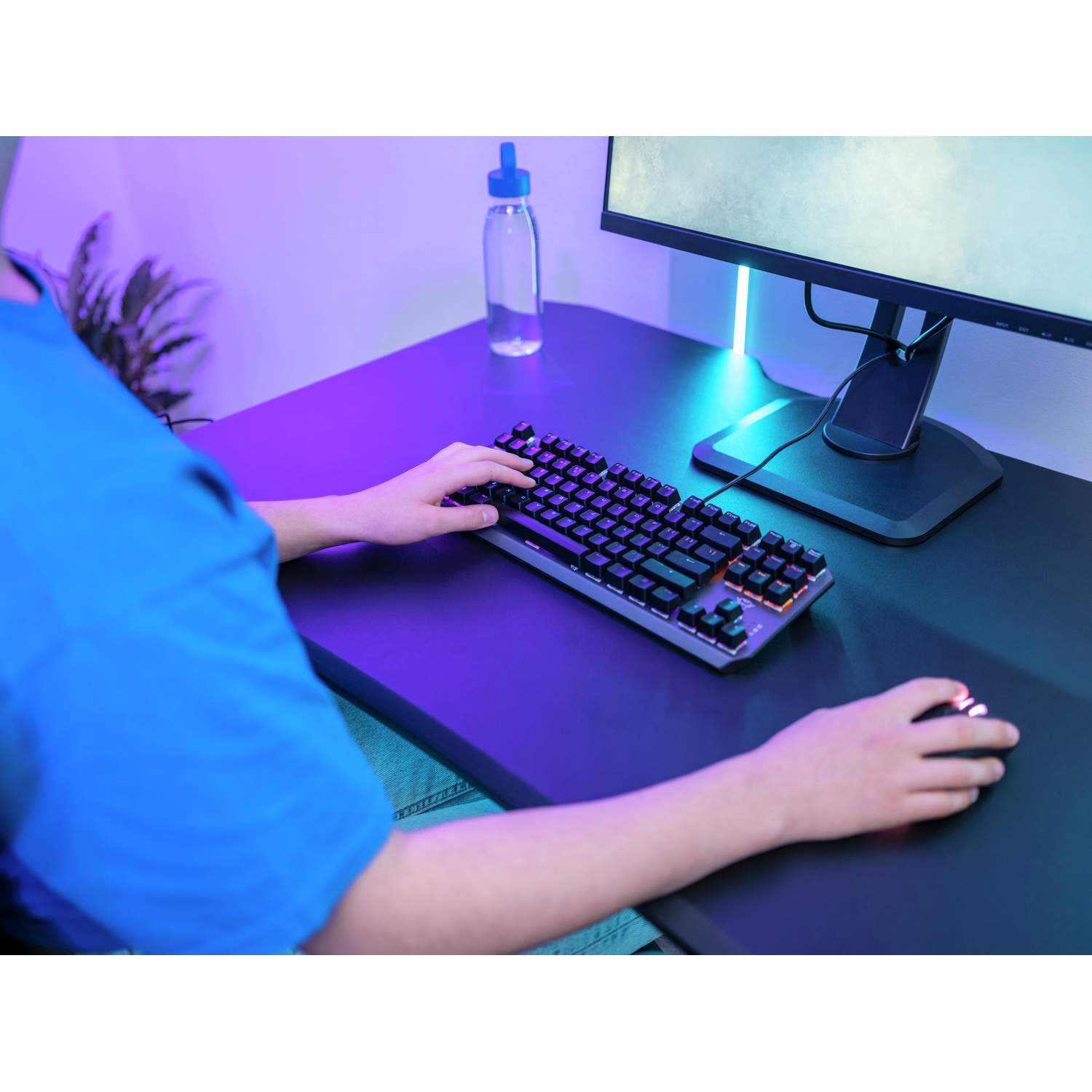 Person using a mechanical keyboard with backlit keys. A computer monitor and water bottle are in the background.