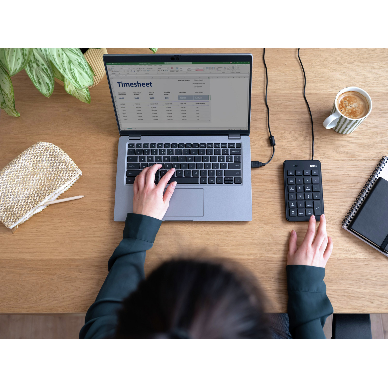 Hands using keyboard and number pad on a desk with laptop, coffee and accessories.