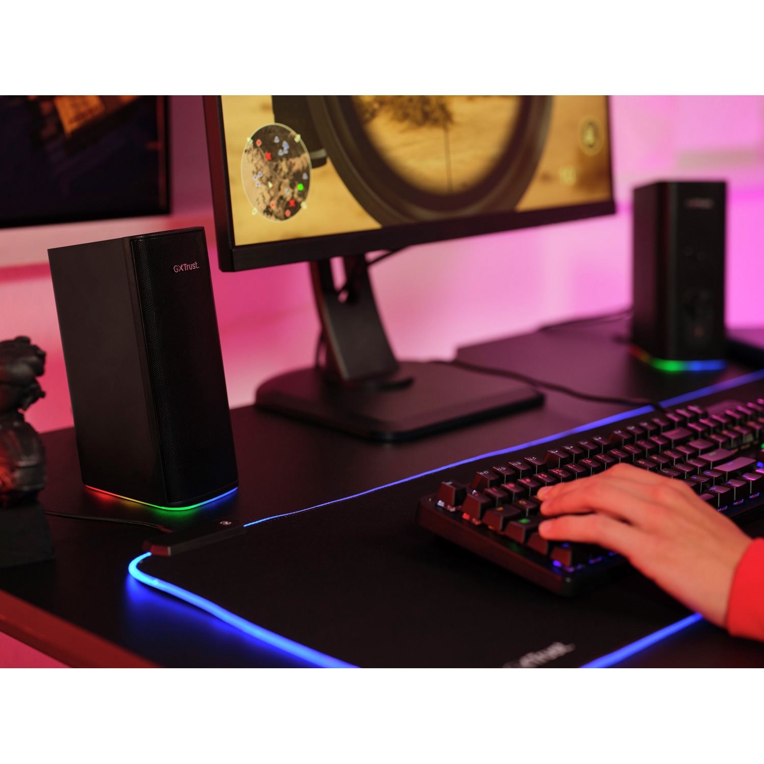 Speakers, monitor, and keyboard on a black desk, with a colorful lighting effect.