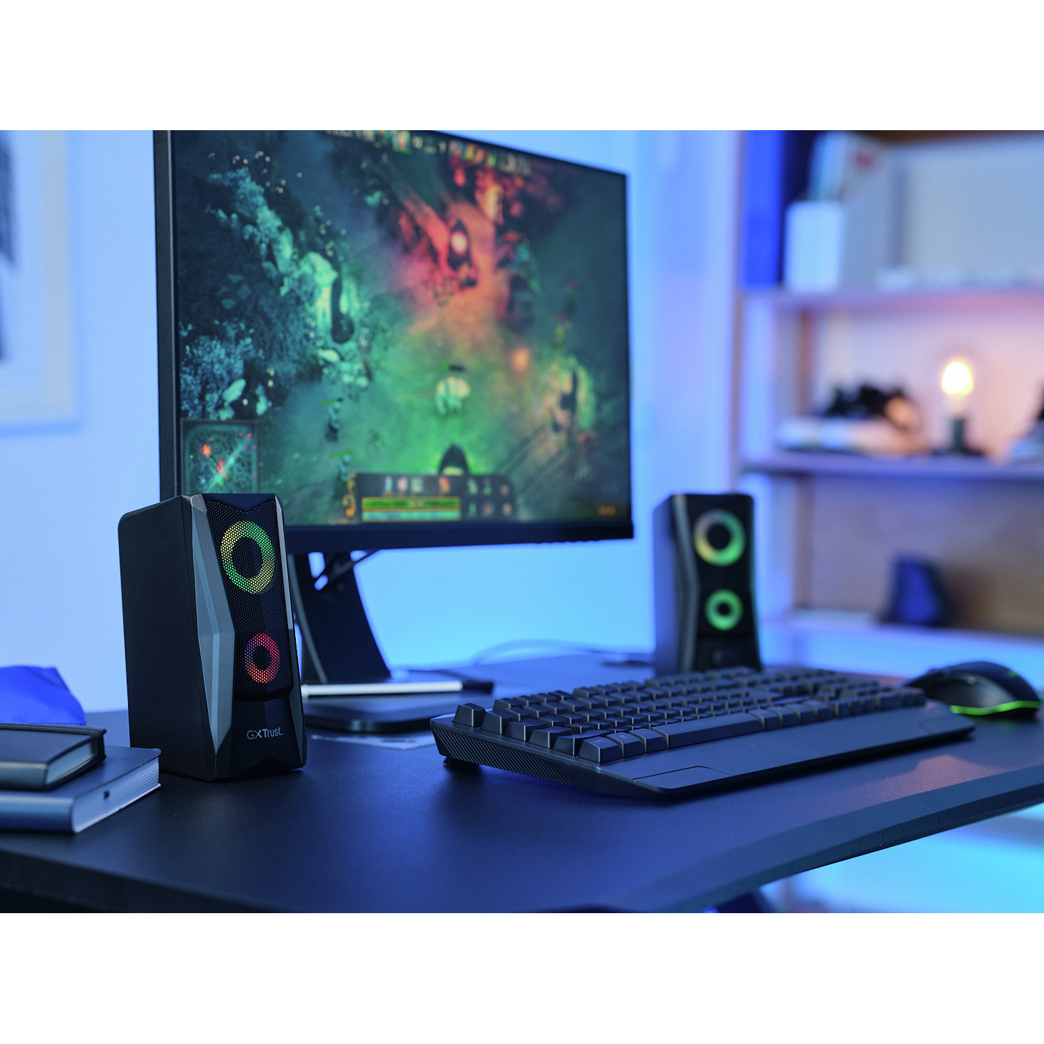 Black speakers with RGB lights, a monitor displaying a game, keyboard, and mouse on a desk.