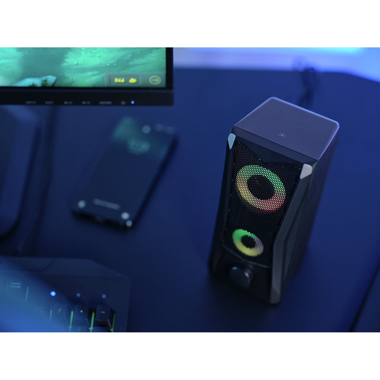 Speaker, monitor, and phone on a dark blue desk. Colorful lighting effects.