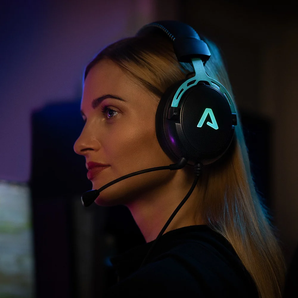 Nő gamer headsettel és mikrofonnal, számítógépen játszik egy sötét szobában.