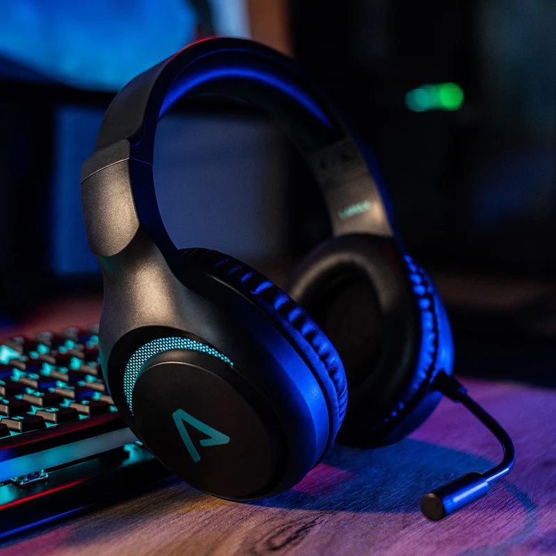 Gamer fejhallgató fa asztalon, billentyűzettel, sötét szobában, kék fénnyel.
