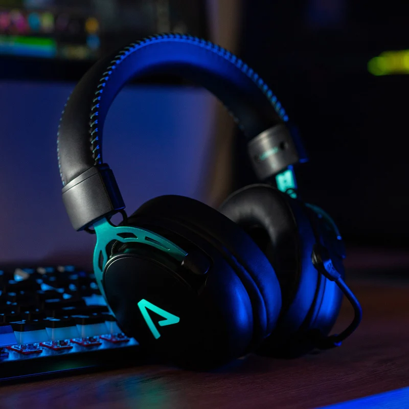 Gaming headset az asztalon. A headset türkiz díszítéssel rendelkezik, a billentyűzet és monitor közelében.