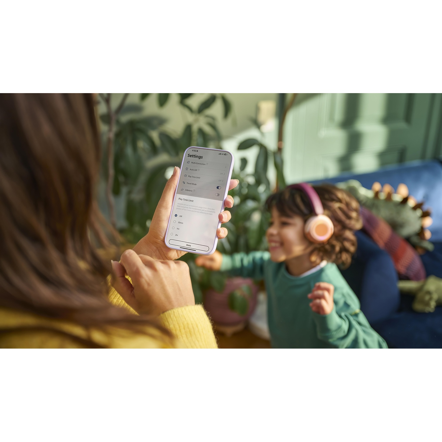 Donna e bambino con telefono e cuffie, in un soggiorno.